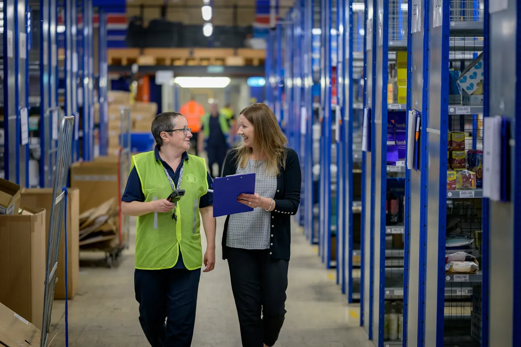 A manager and a colleague reviewing a clipboard while walking through a stock aisle