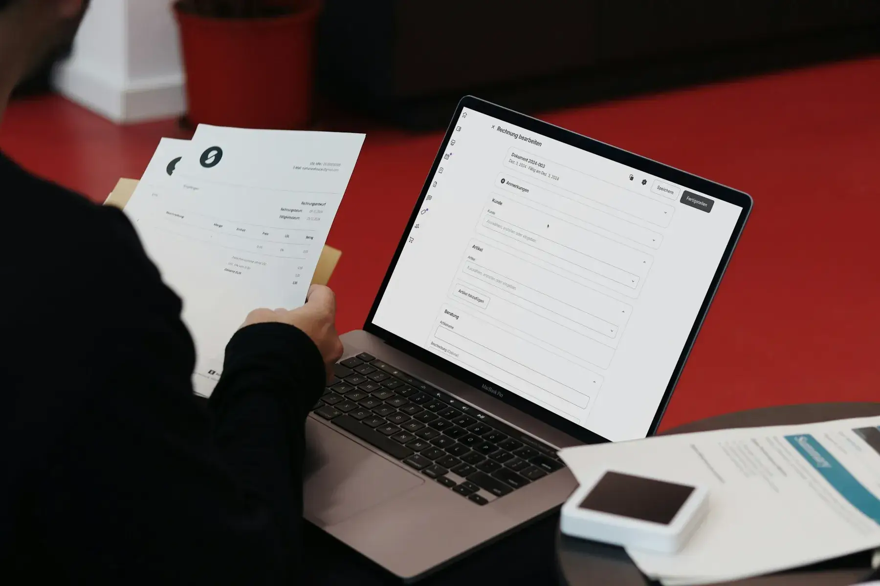A paper supplier invoice held beside a laptop