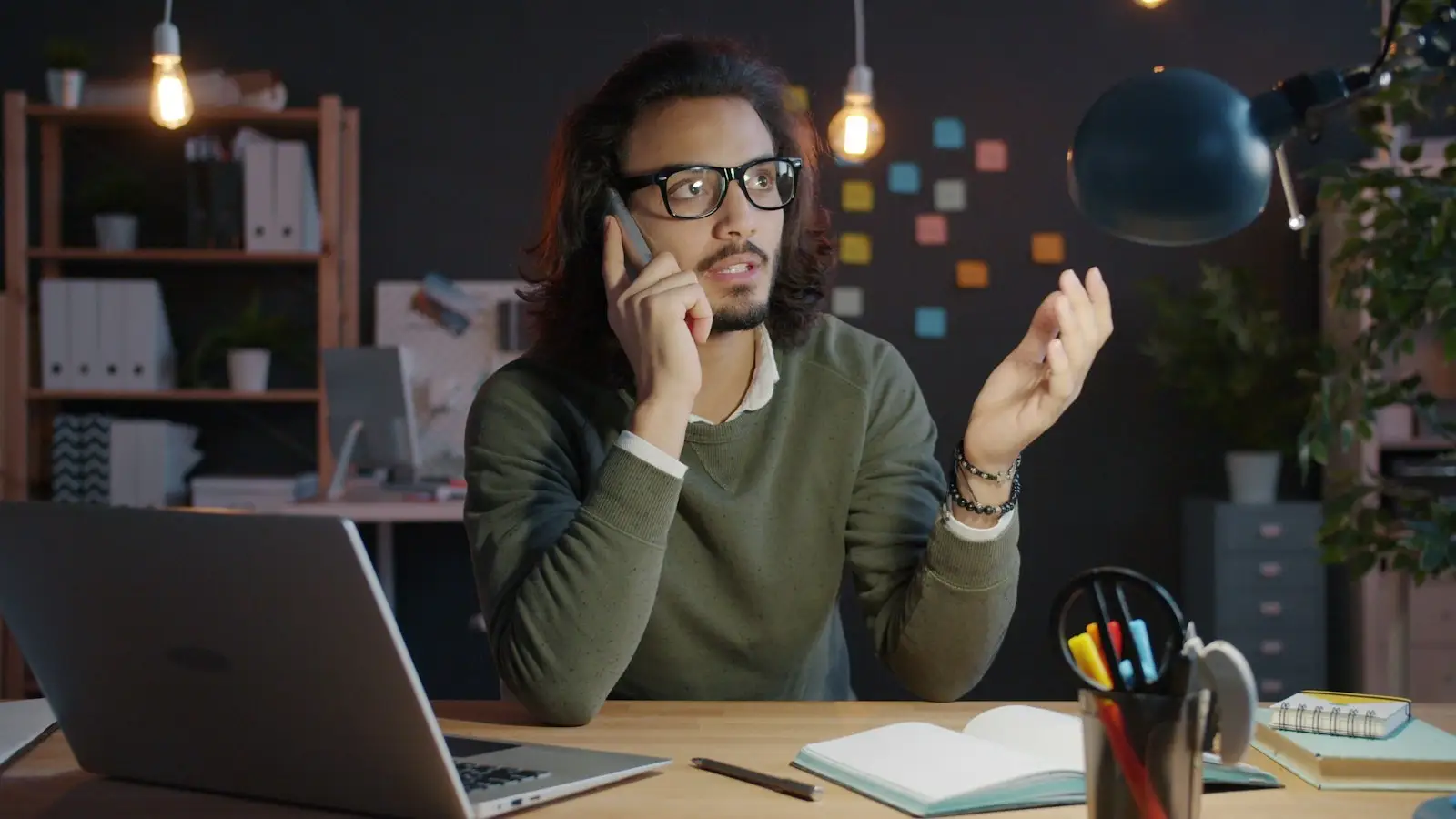 A man on a phone call at his desk beside a laptop